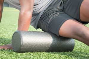 picture of a male african american athlete massaging their musle on a foam roller. 